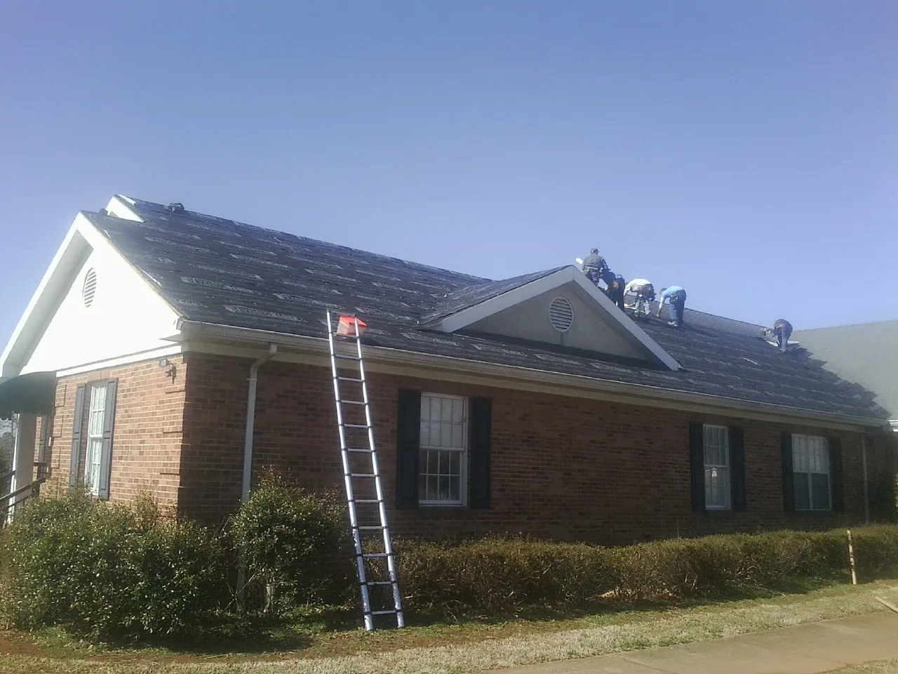 Crew tearing shingles off a brick ranch roof with a ladder set — Emergency Roof Repair work by our crew in Shields