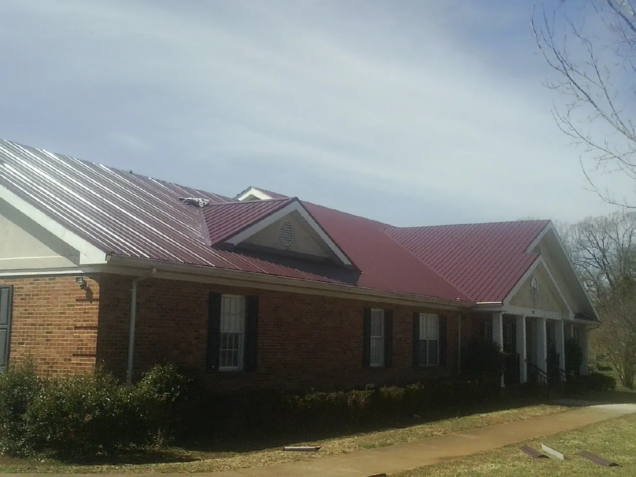 Red metal roof with gabled entries on a long brick building, from a Hail Damage Roof Repair job in Shields